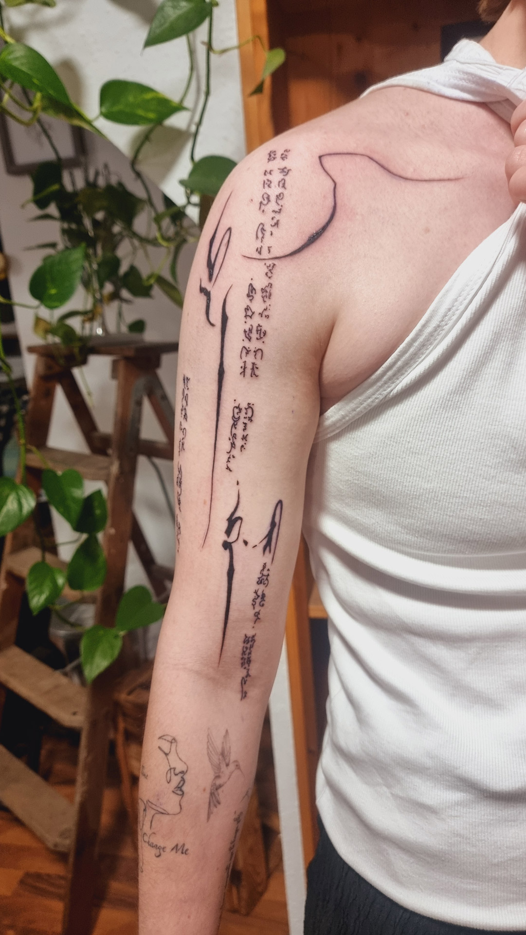 Person laechelt, weiss, Arm mit schwarzem Schrift Tattoo und Linie