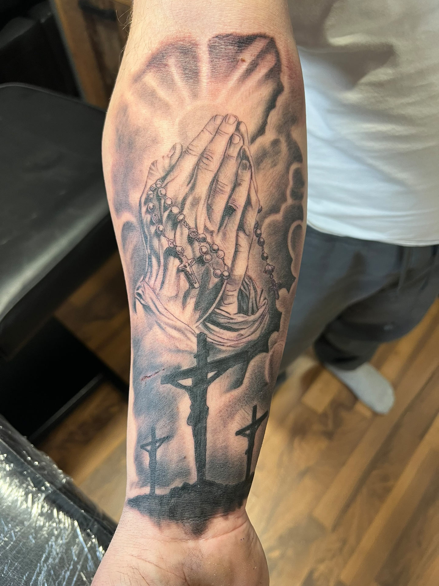 Unterarmtattoo mit betenden Haenden und Rosenkranz in Grau Schwarz mit Kreuzen