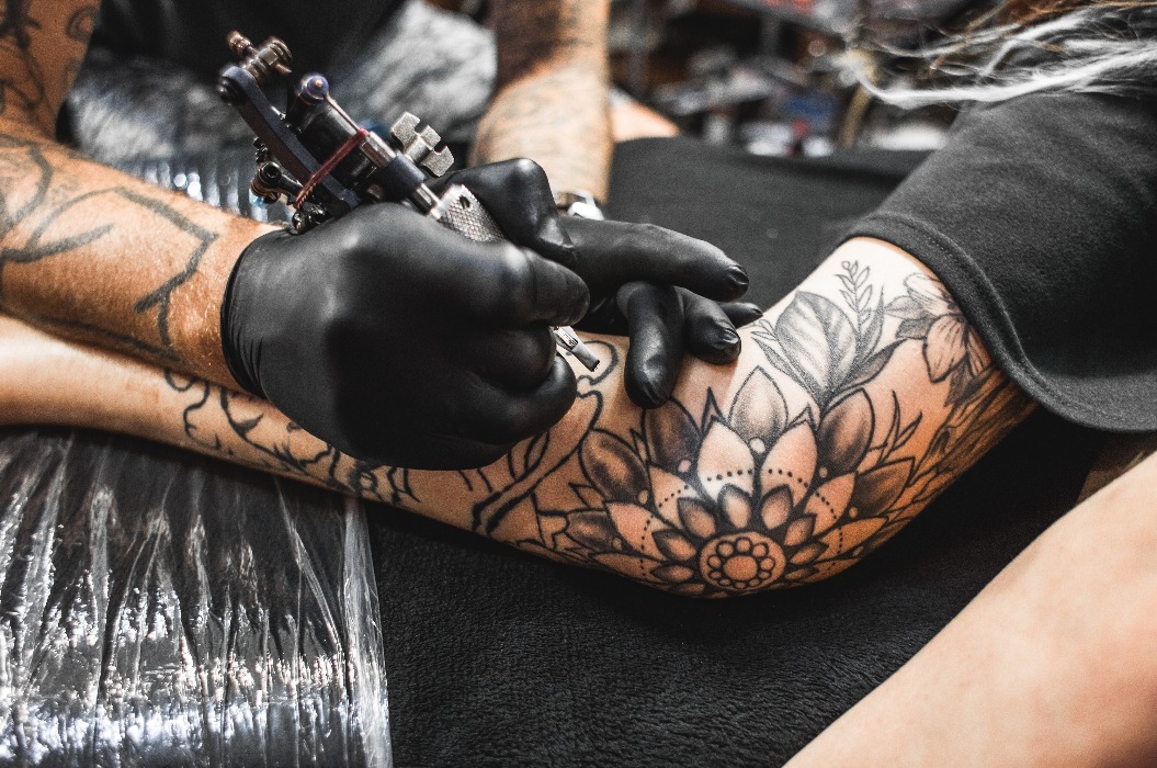 Ein Mädchen mit Dreadlocks in einem Tattoo-Studio. Der Meister gestaltet ein Motiv auf dem Körper eines jungen, hübschen Mädchens. Nahaufnahme der Hände und der Tätowiermaschine