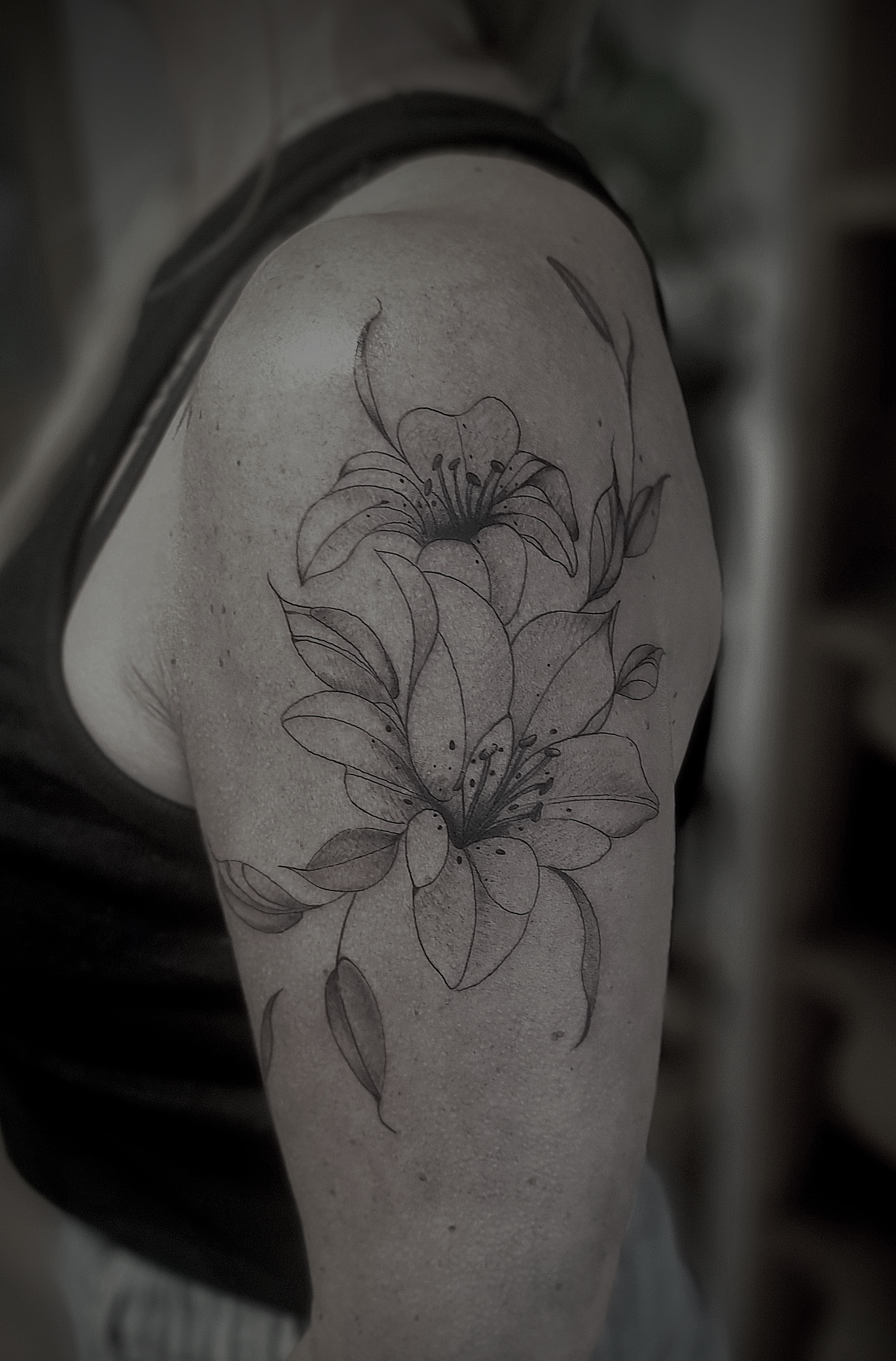 Feines Lilien Tattoo in Schwarz auf der Schulter einer Person