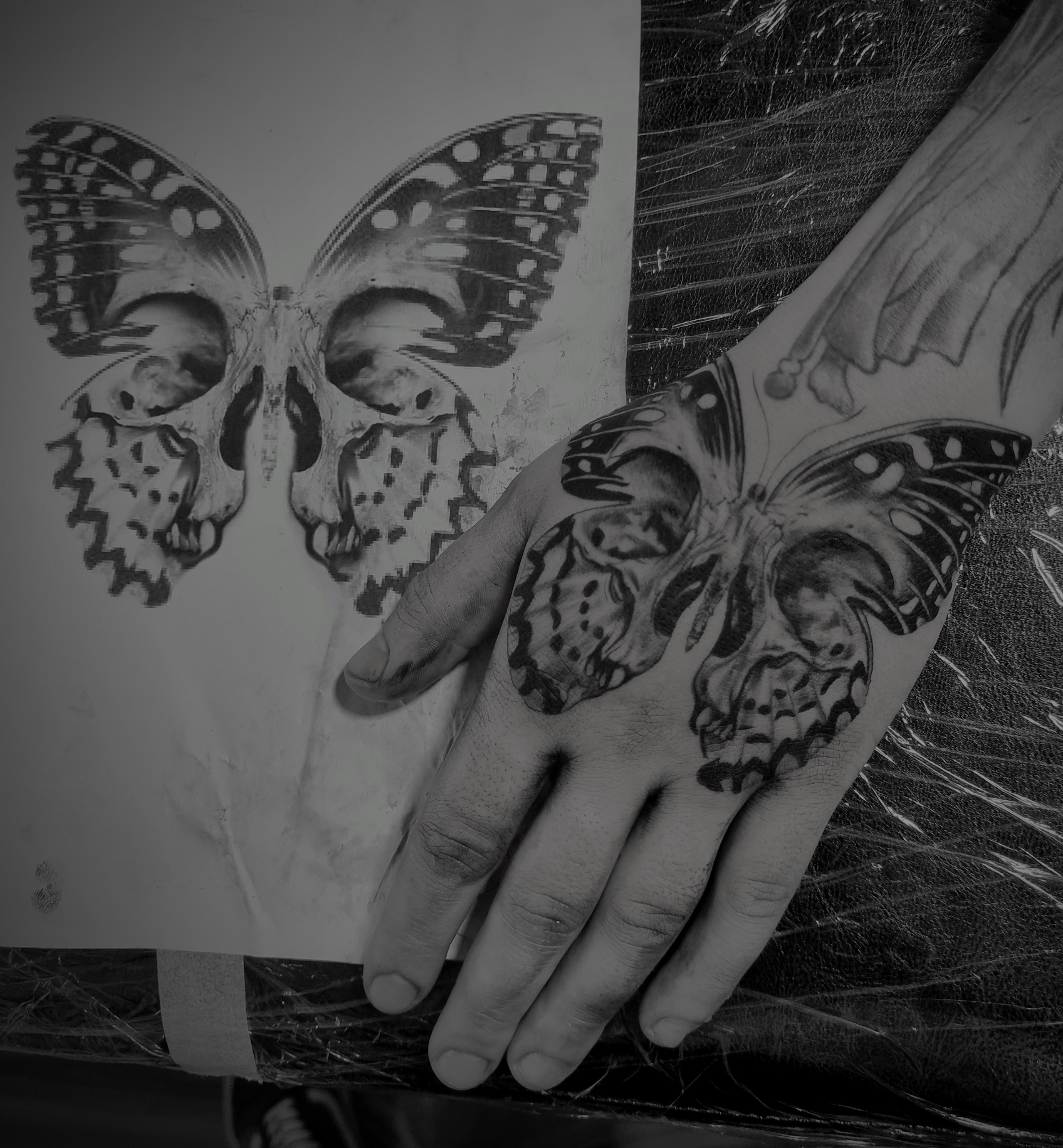 Hand mit Schmetterling Totenkopf Tattoo neben passender Vorlage in Schwarzweiss