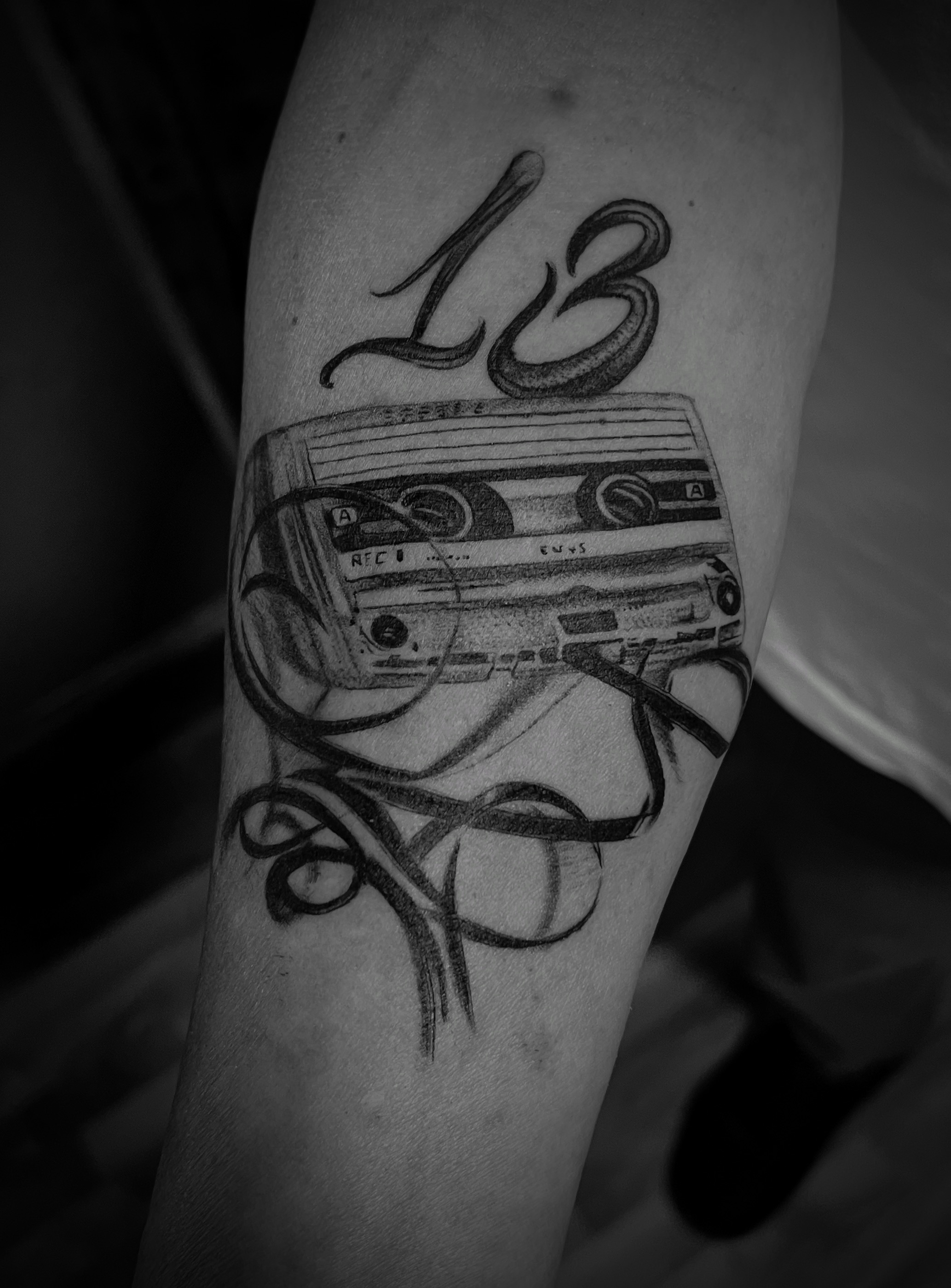 Schwarzweiss Tattoo einer Kassette mit heraushaengendem Band und der Zahl 13