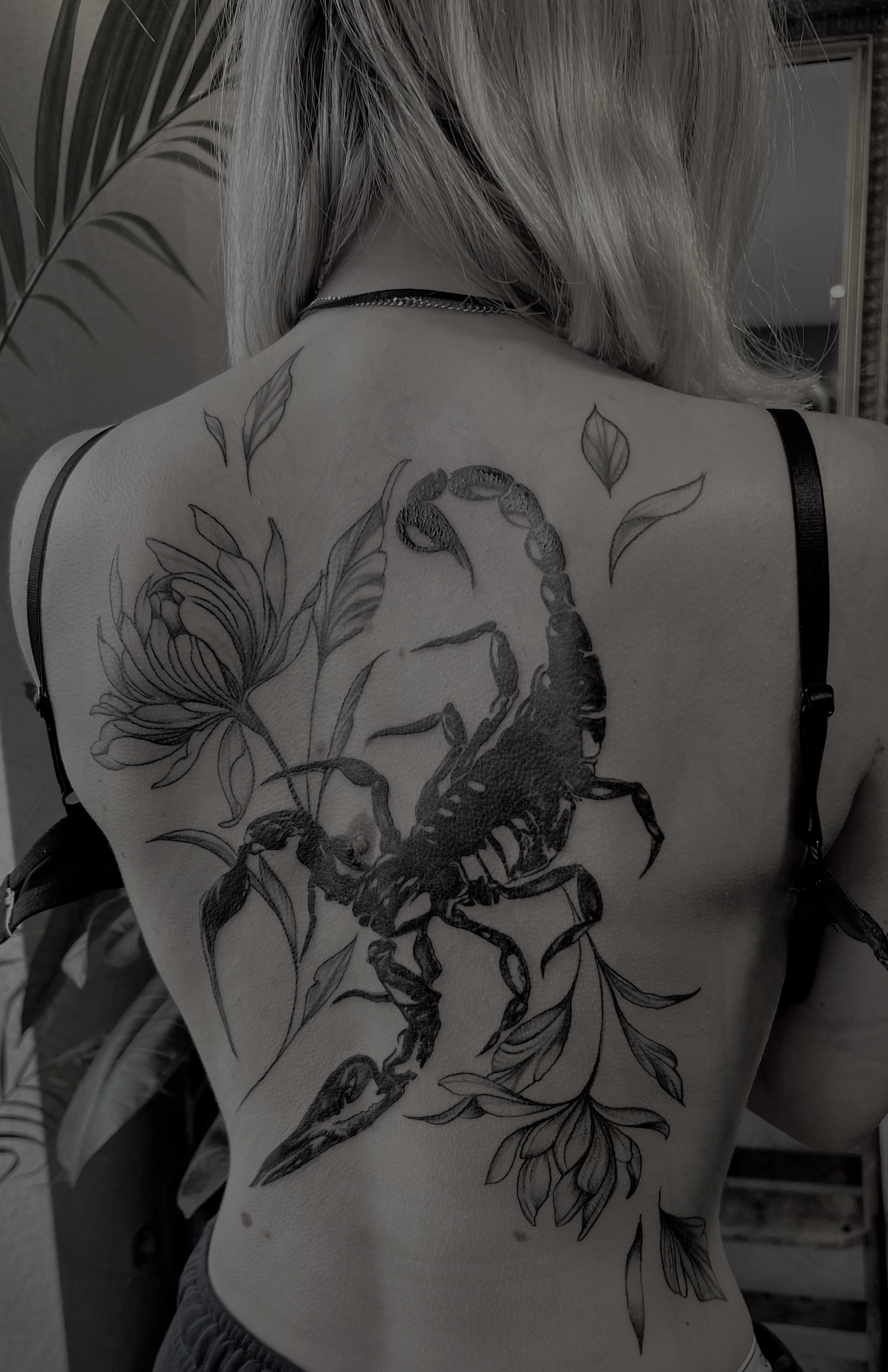 Blonde Frau von hinten mit grossem Skorpion und Blumen Tattoo auf dem Ruecken